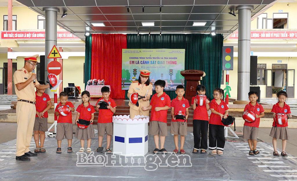 Cán bộ cảnh sát giao thông hướng dẫn các em nhỏ cách đội mũ bảo hiểm đúng quy cách.