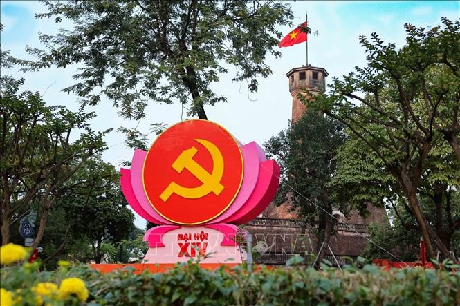 Biểu tượng b&uacute;a liềm tr&ecirc;n đ&agrave;i sen hồng nổi bật trước Cột cờ H&agrave; Nội (khu vực đường Điện Bi&ecirc;n Phủ), kết hợp vẻ đẹp lịch sử h&agrave;o h&ugrave;ng với kh&ocirc;ng kh&iacute; ch&iacute;nh trị trang nghi&ecirc;m.