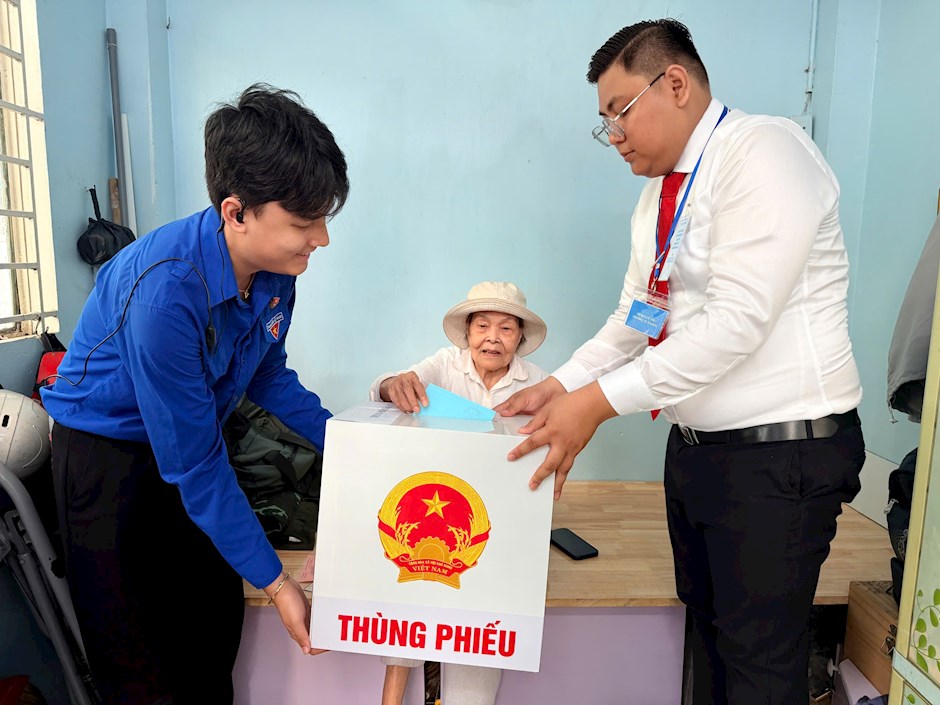 Cử tri Nguyễn Thị Liễu (sinh năm 1944, khu phố 7, phường Xuân Hòa) dù tuổi cao và đau chân vẫn cùng người thân đến khu vực bỏ phiếu số 2 tại Trường Mầm non Tuổi Thơ 7. Lực lượng hỗ trợ mang thùng phiếu phụ để cử tri thực hiện quyền công dân tại chỗ. Ảnh: HOÀNG HÙNG